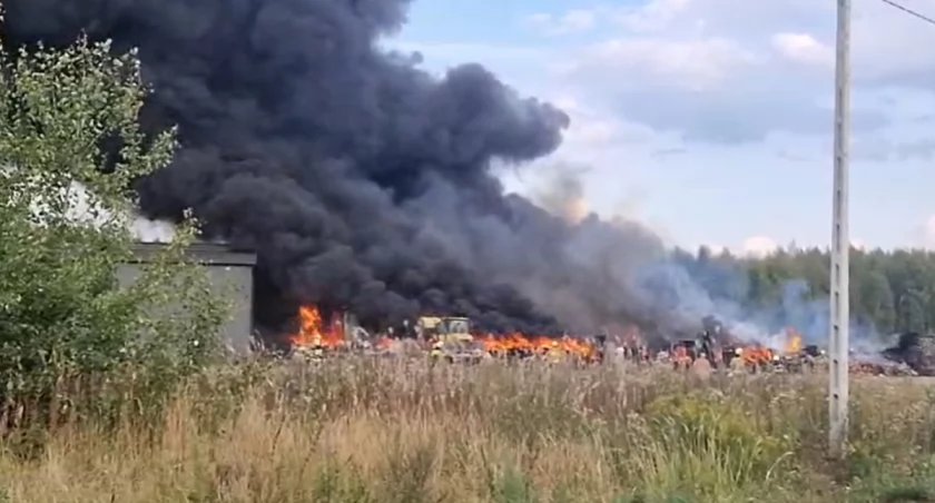 Zmęczeni strażacy po walce z ogniem w Ławkach. W tle wciąż płonie baza transportowa
